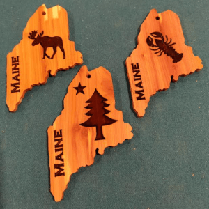 Handcrafted aromatic cedar ornaments featuring the 1901 Maine flag, Maine lobster or a Moose.